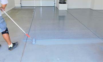 contractor using paint roller to apply color to concrete before application of clear epoxy coating.