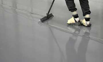 contractor pushing extra gray epoxy across floor with roller