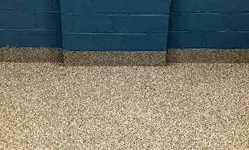 tan epoxy flooring in a highschool; pictured against a blue brick wall.